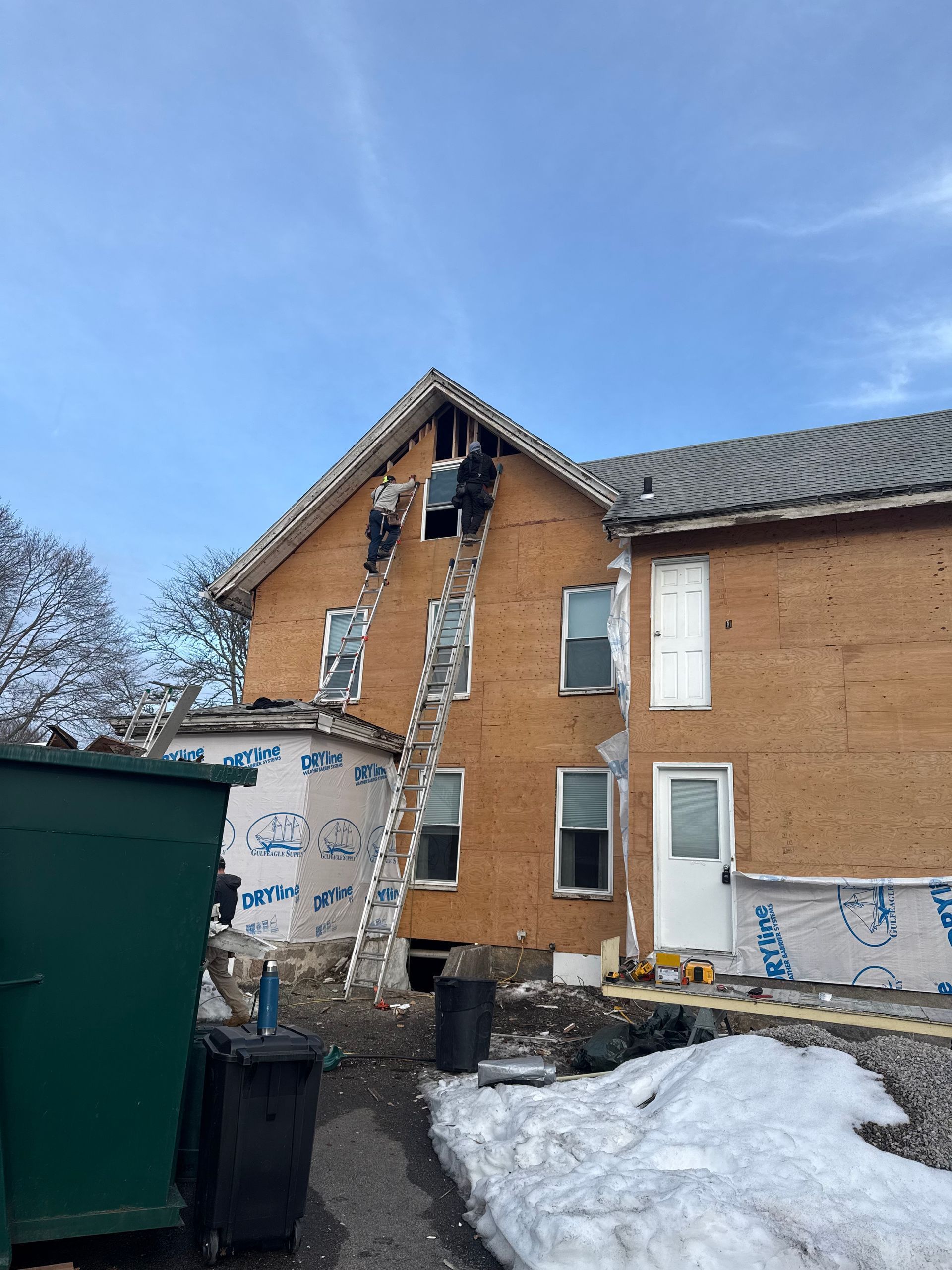People on ladders working on the side of a building, under a blue sky.