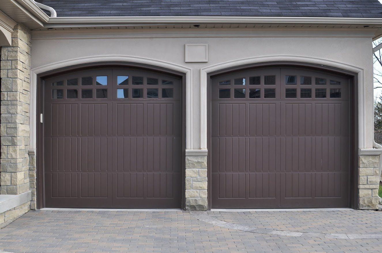 Two brown garage doors with arched tops, stone columns, and tan trim.