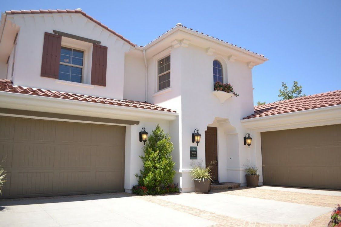 White stucco house with brown garage doors, red tile roof, and a blue sky.