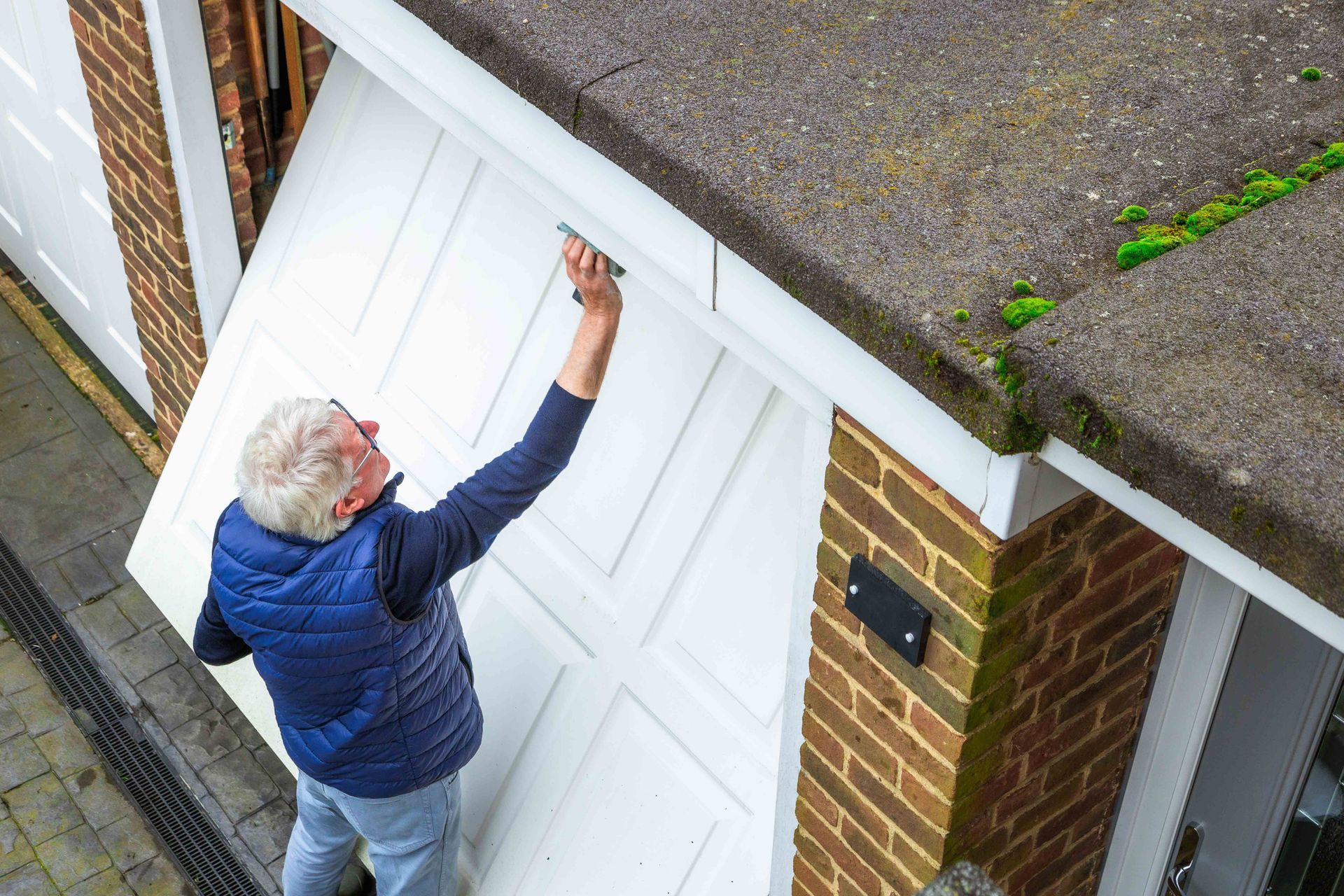 Man opening white garage door. Brick building, concrete roof.