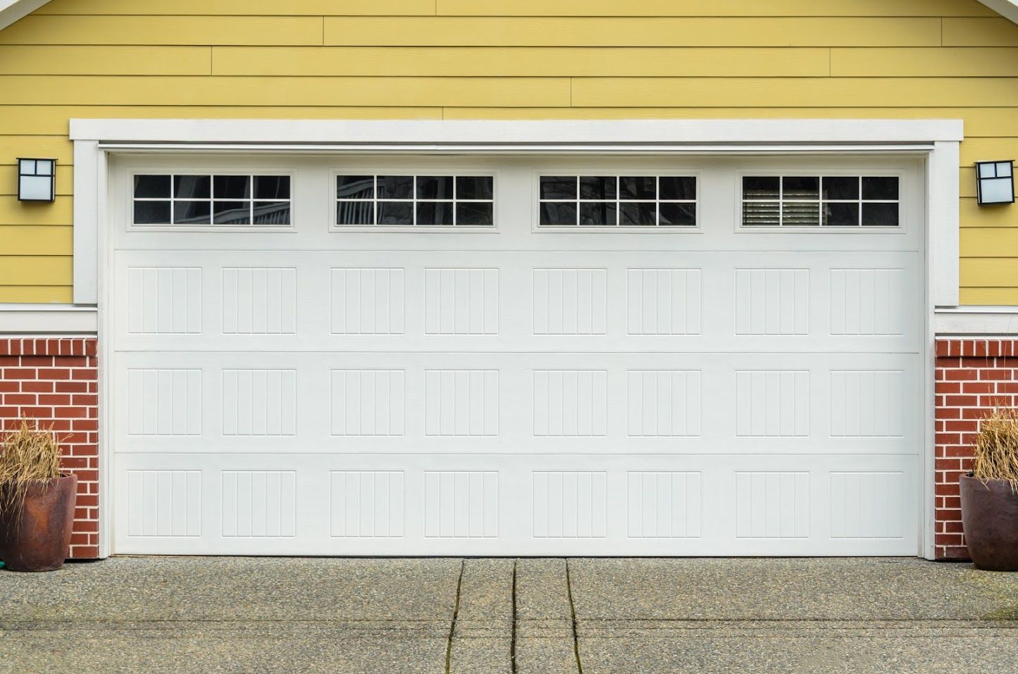 White garage door with windows, on a yellow house with brick accents, and concrete driveway.