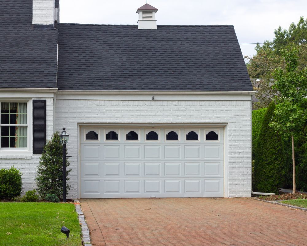 White painted brick garage with black roof and brick driveway.