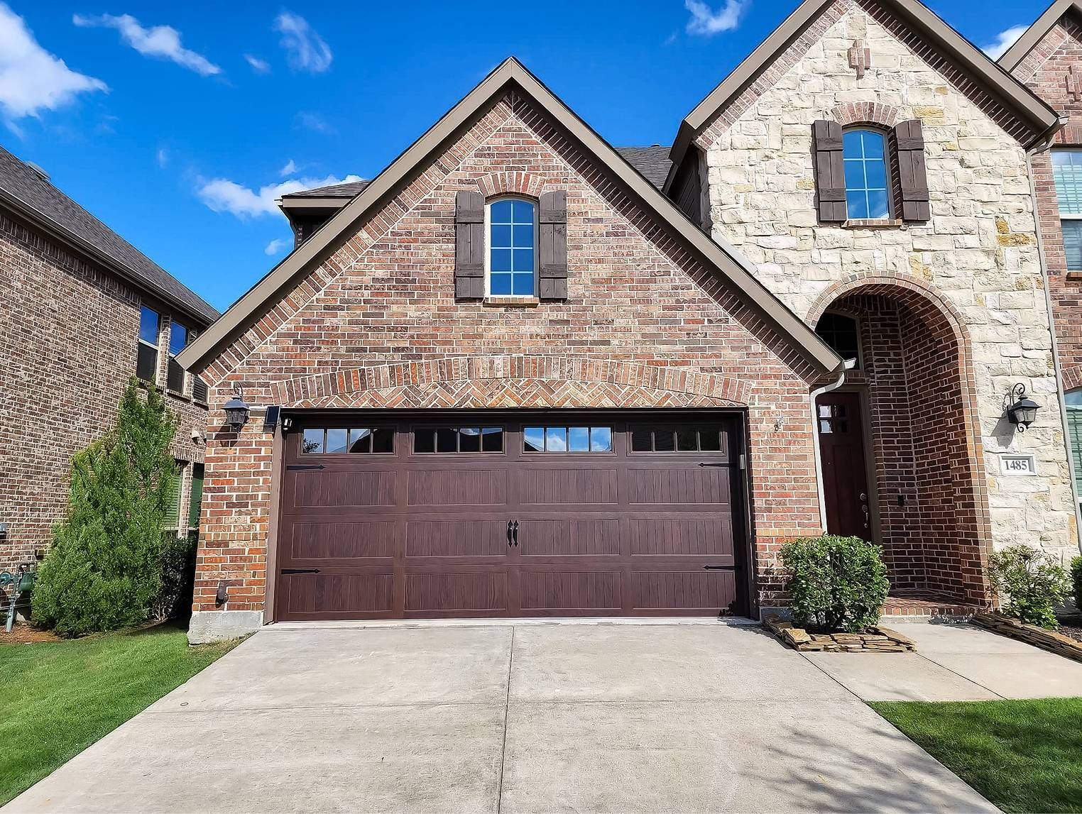Brown brick house with a brown garage door. Blue sky. Concrete driveway.