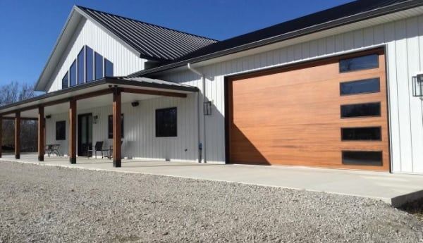 White building with a brown garage door and porch, under a clear blue sky.