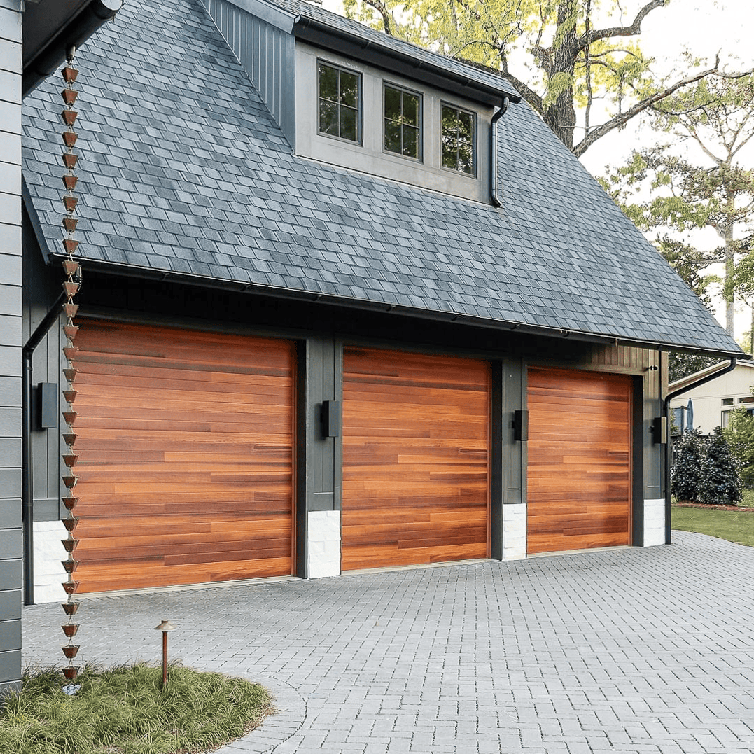 Three-bay garage with wooden doors, gray roof, and brick driveway.