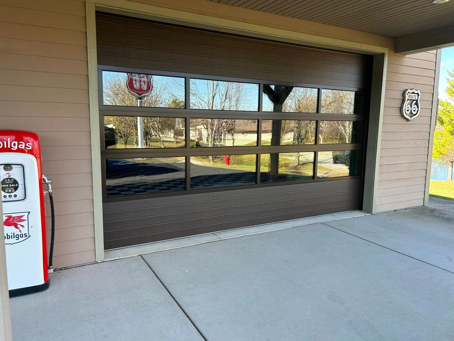 Brown glass garage door reflecting a street scene, with a vintage gas pump and Route 66 sign.