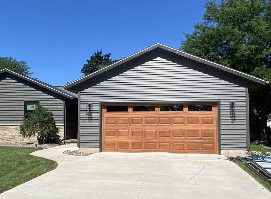 Garage with brown door, gray siding, and a concrete driveway on a sunny day.