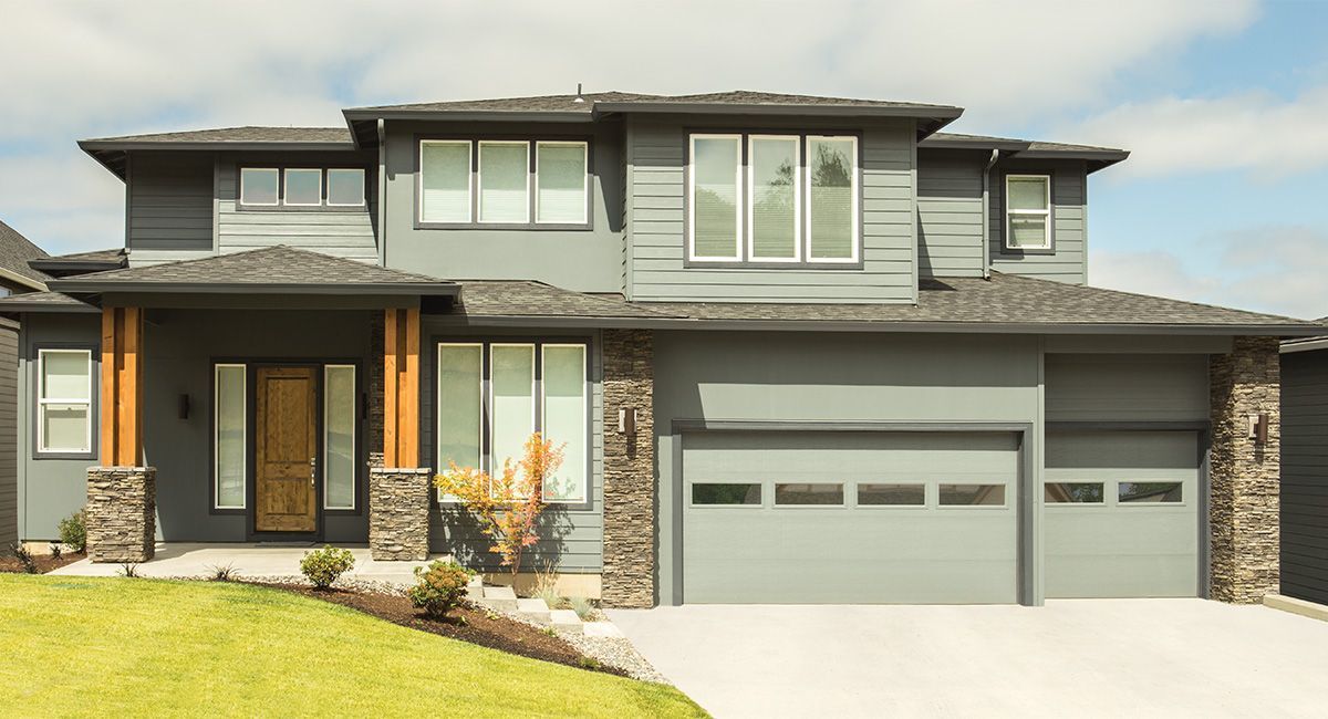 Gray two-story house with stone accents, a two-car garage, and a green lawn.