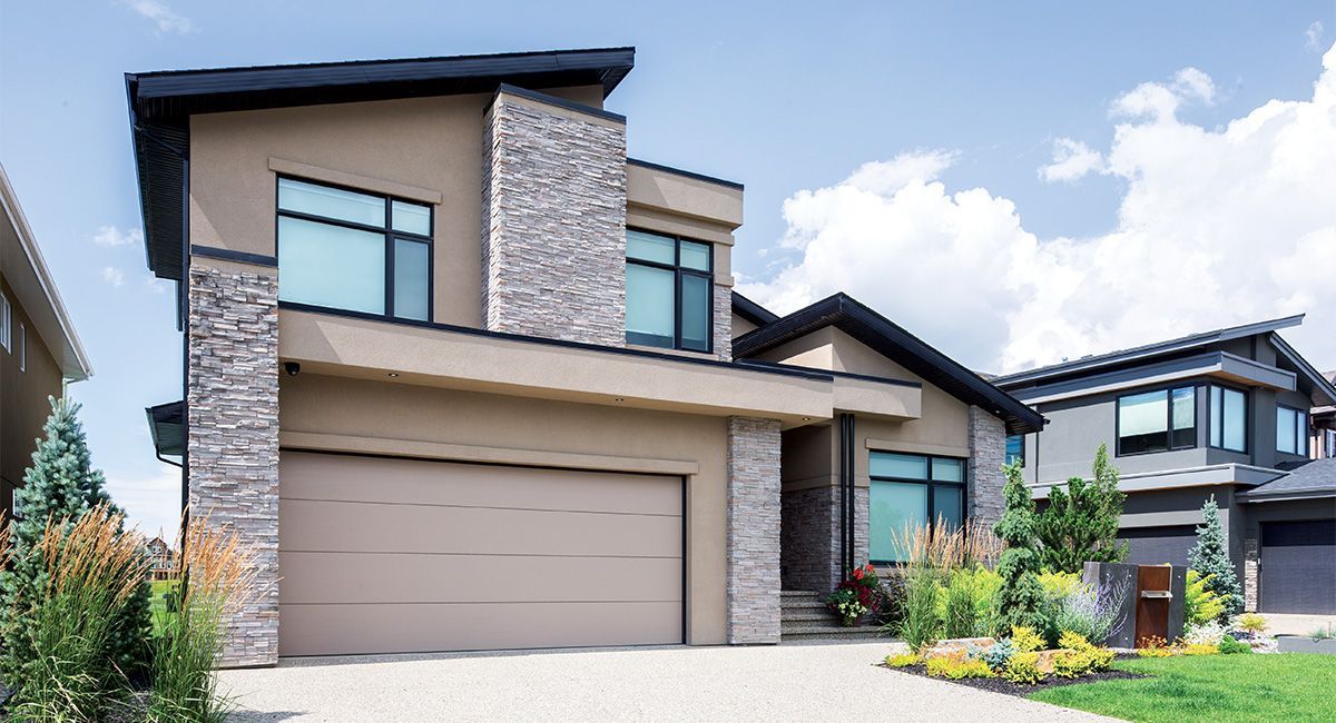 Modern two-story house with beige stucco and stone accents, two-car garage, and landscaped yard.