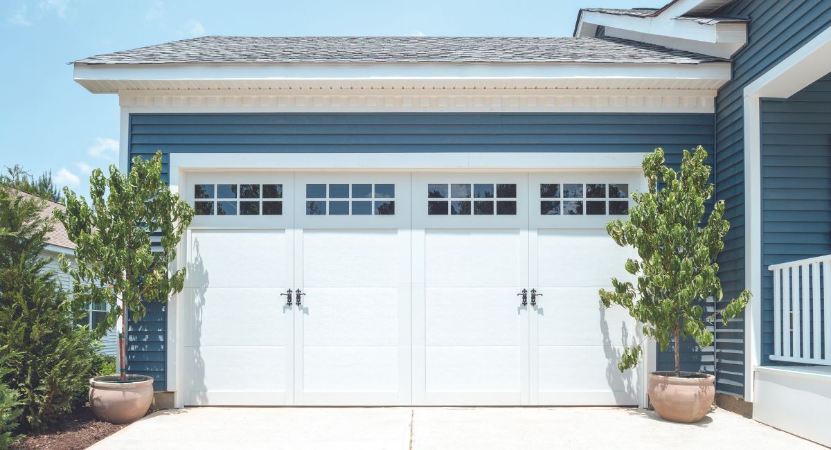 White double garage door with windows, blue siding, and potted trees.