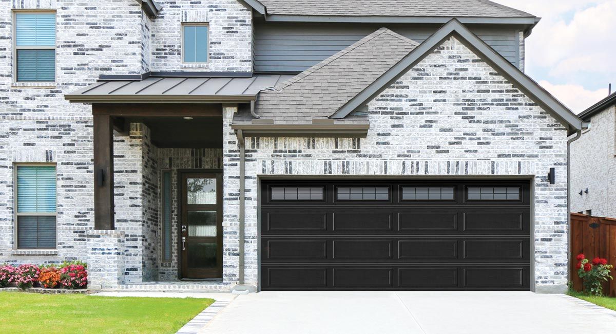 Black garage door on a house with gray brick and roof; driveway and green lawn.
