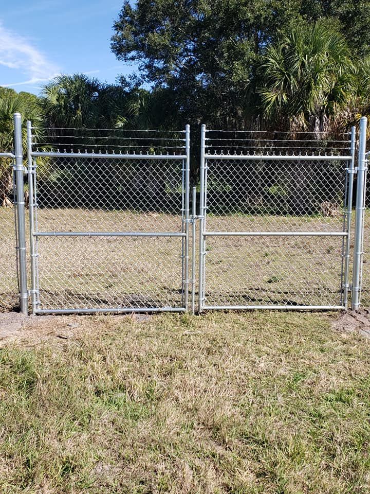 A chain link fence with a gate in the middle of a grassy field.