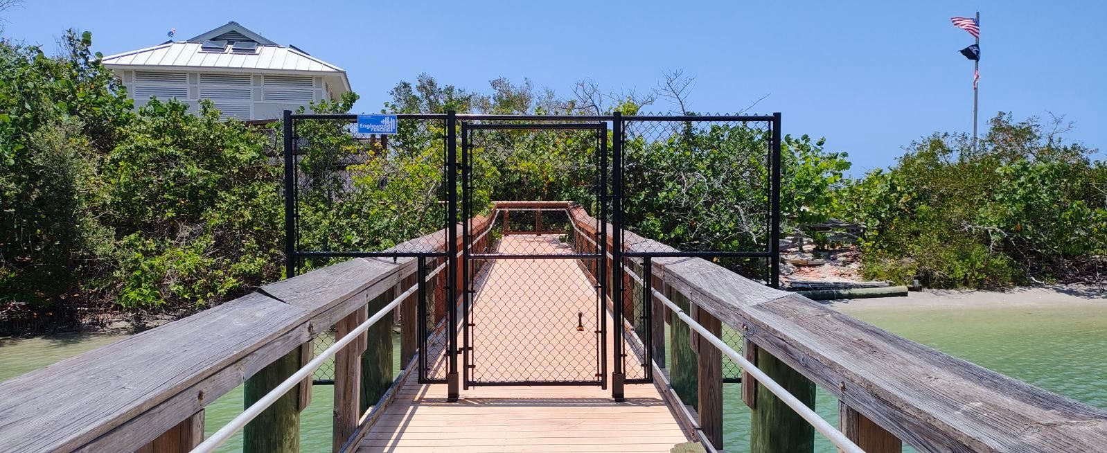 A wooden dock with a chain link fence leading to a house.