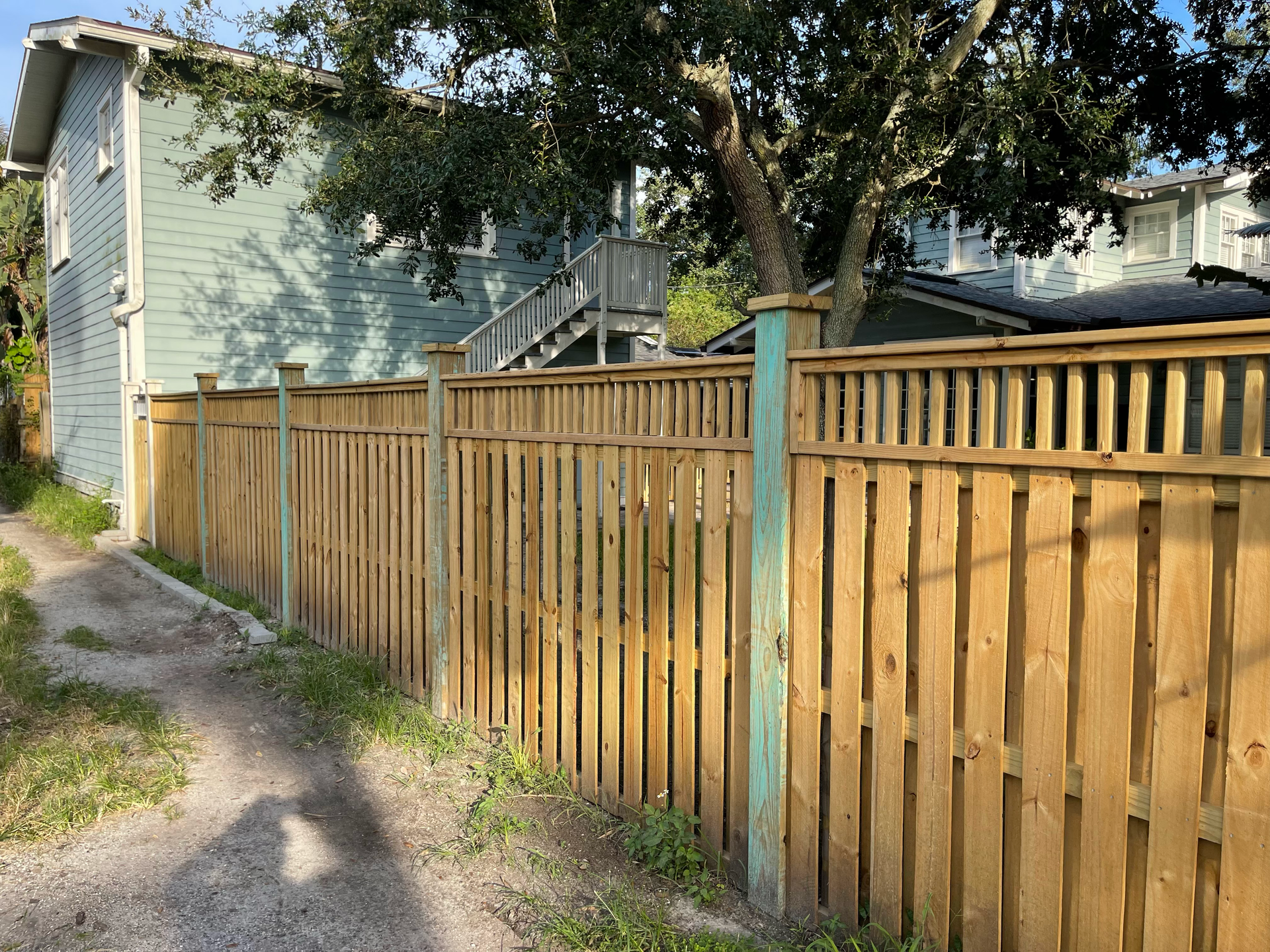 A wooden fence surrounds a dirt road in front of a house.
