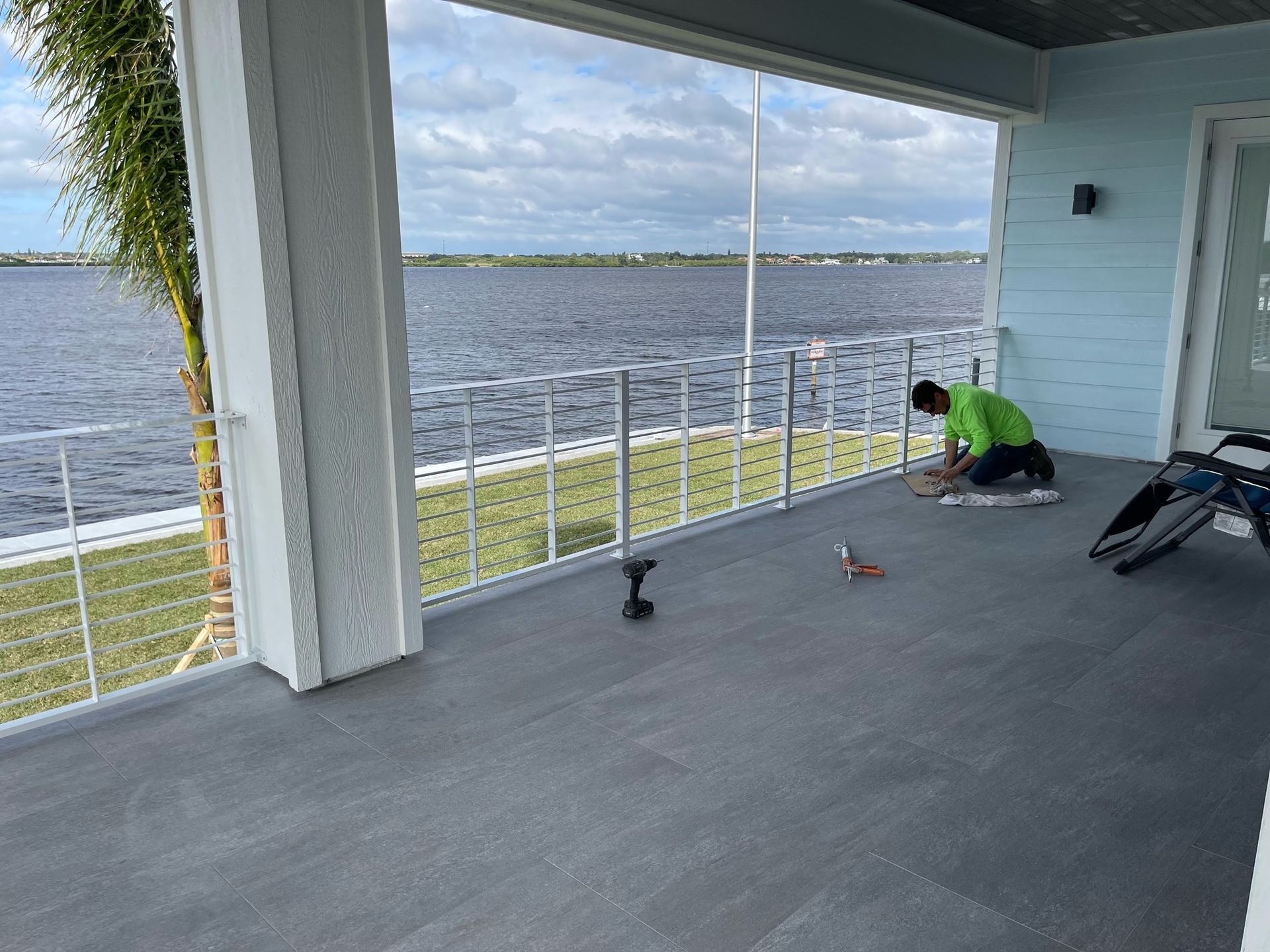 A man is working on a balcony overlooking a body of water.