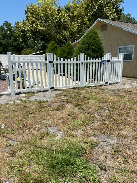 A white picket fence surrounds a grassy yard in front of a house.