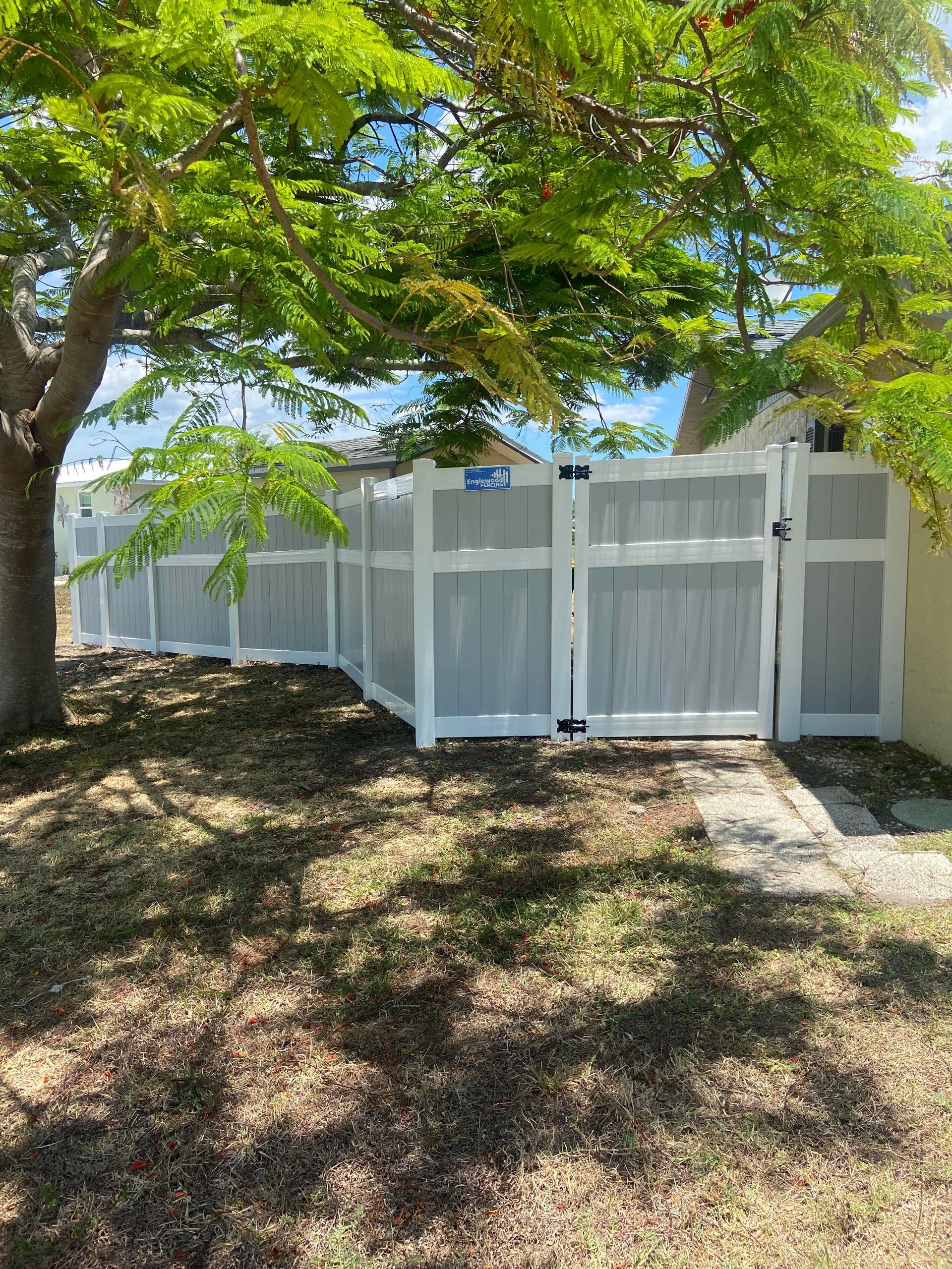 A white fence with a gate and a tree in the background.