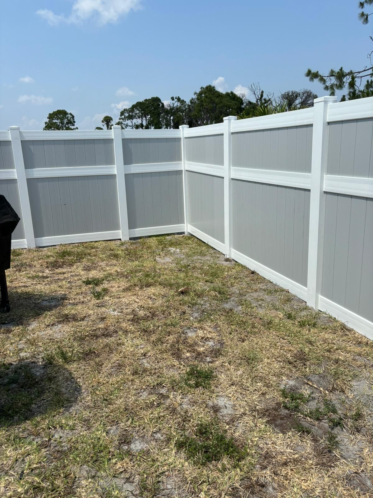 A dog is standing in the grass next to a white fence.