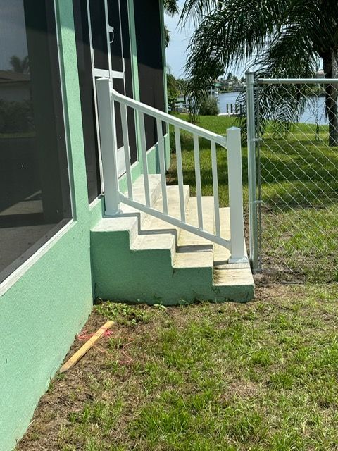 A green house with a white railing and stairs.