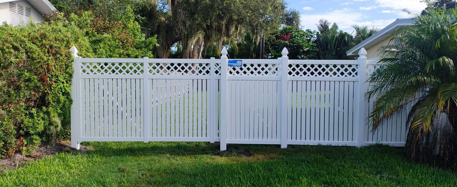 A white fence is sitting in the grass in front of a house.