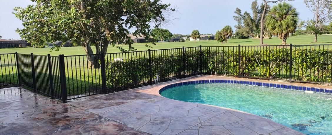 A swimming pool with a fence around it and a golf course in the background.