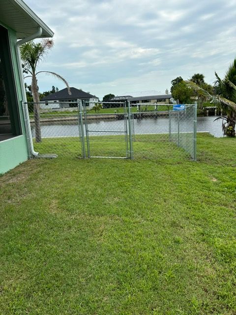 A fence surrounds a lush green yard with a river in the background.