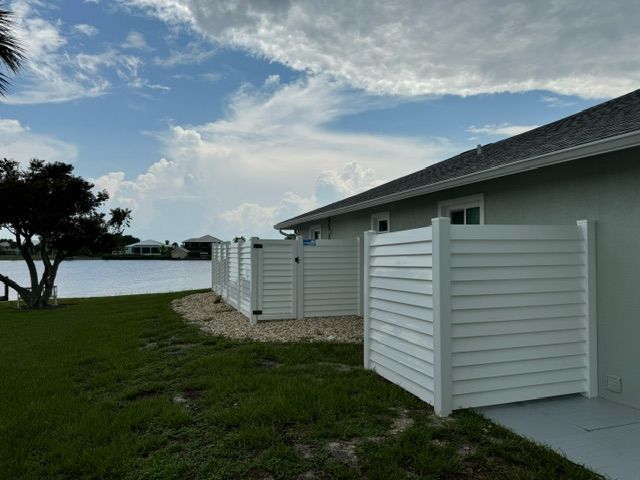 A white fence is in front of a house next to a body of water.