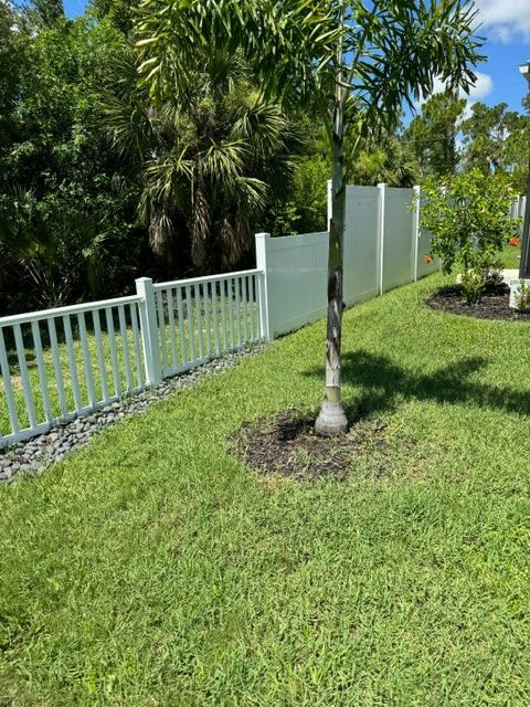 A white fence surrounds a lush green yard with a tree in the middle.