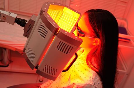 A person receiving red light therapy from a medical device in a clinical setting