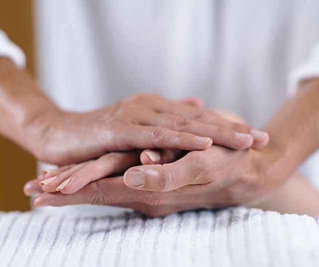 Hands gently stacked on a person’s back during a massage treatment