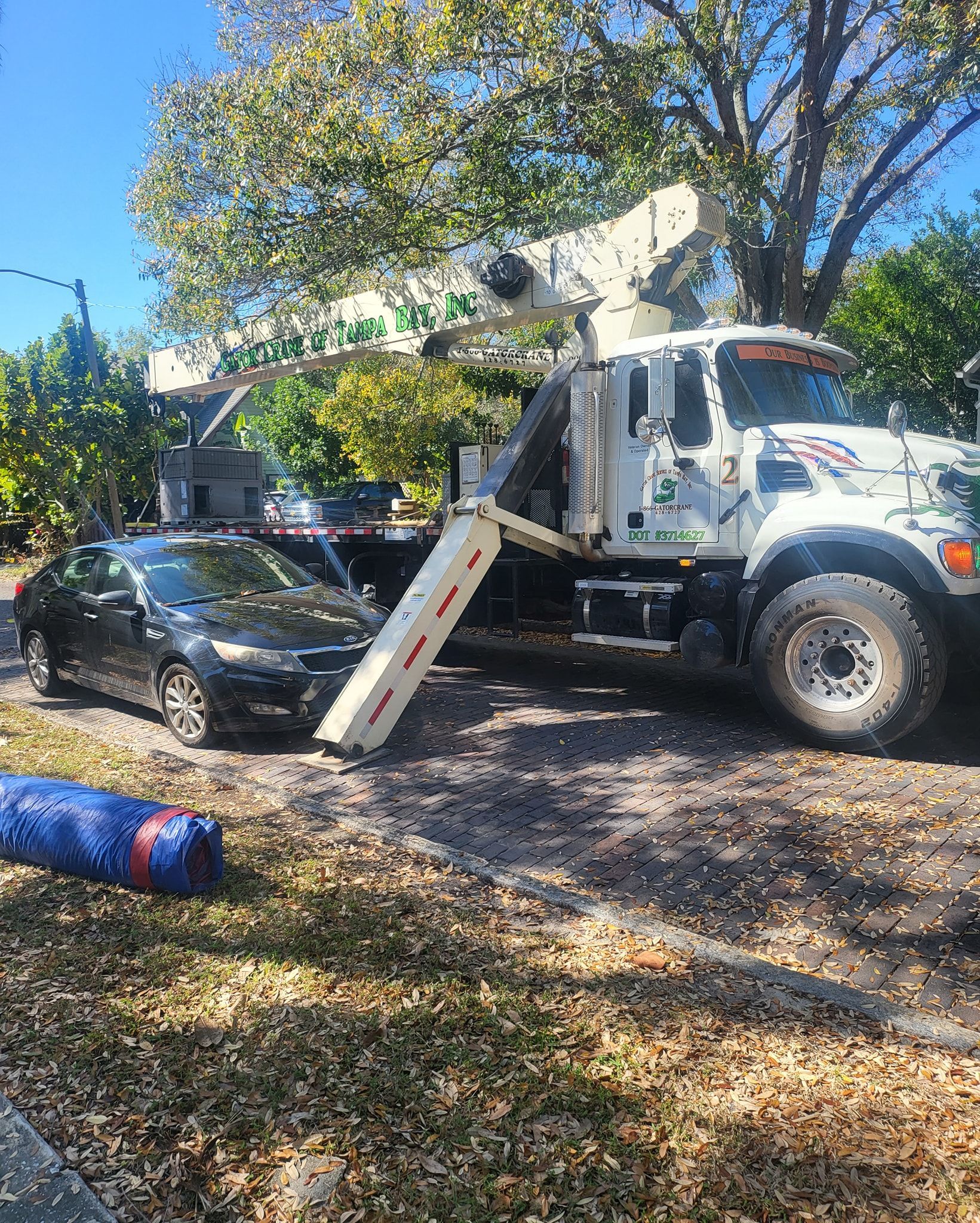 A white truck with a crane on top of it is parked in a driveway next to a car.