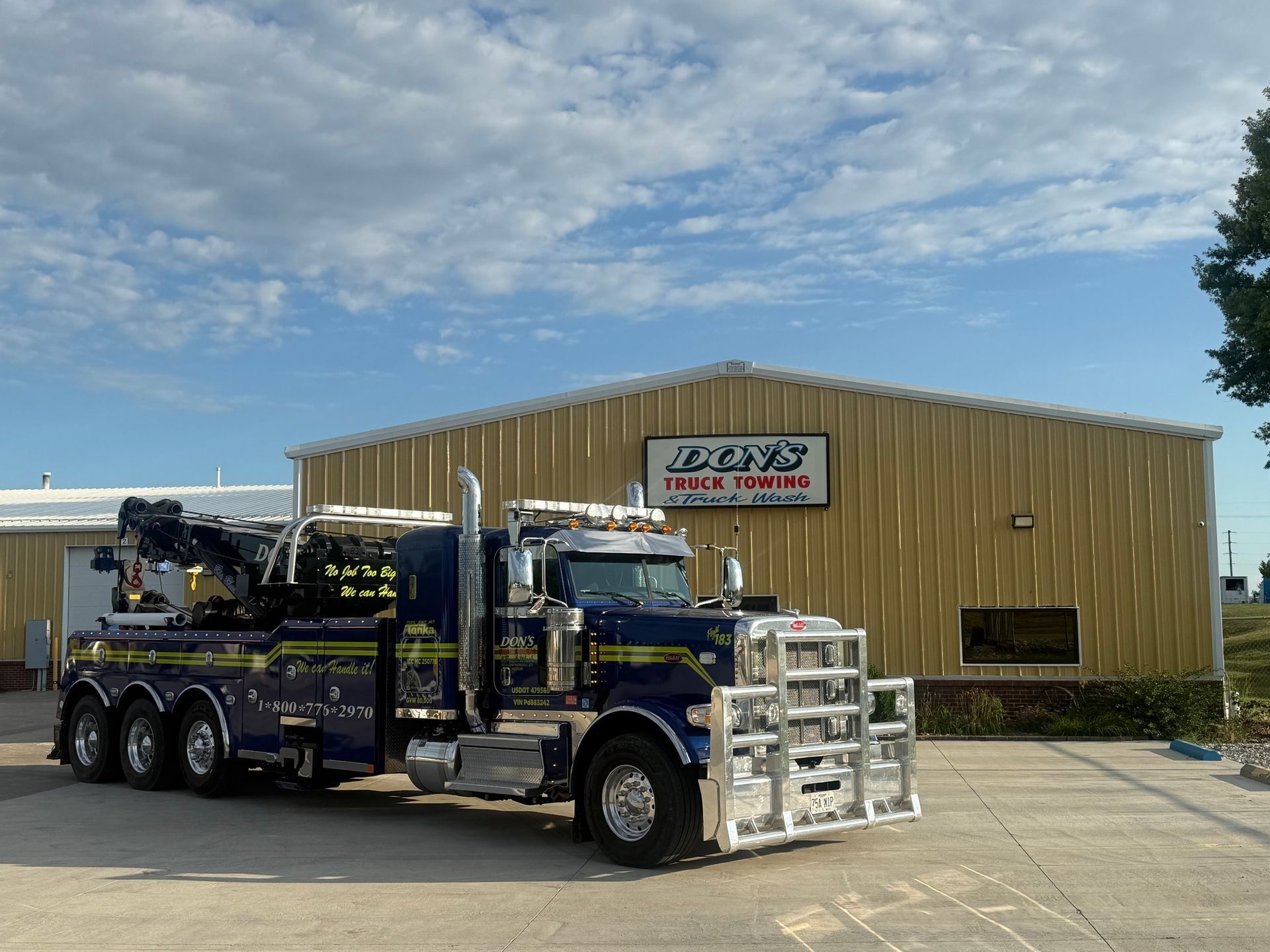 A blue wrecker tow truck with yellow and chrome accents parked outside of the business