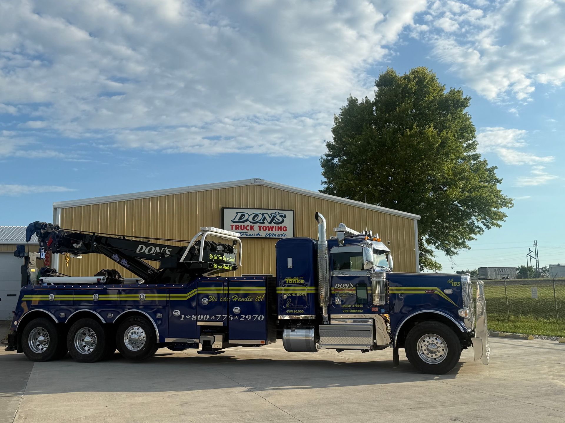 A blue wrecker tow truck with yellow and chrome accents parked outside of the business