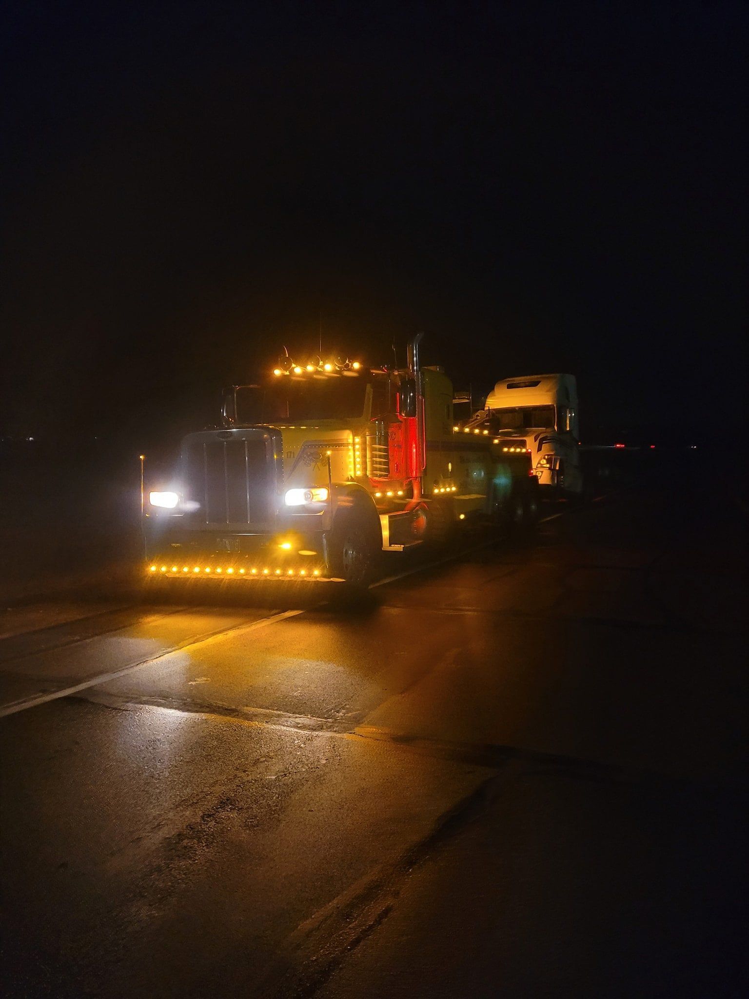 Semi-truck with many lights on a dark road at night.