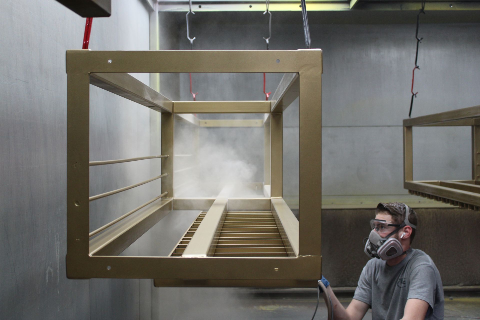 Worker in respirator spraying gold-colored frame in a spray booth.