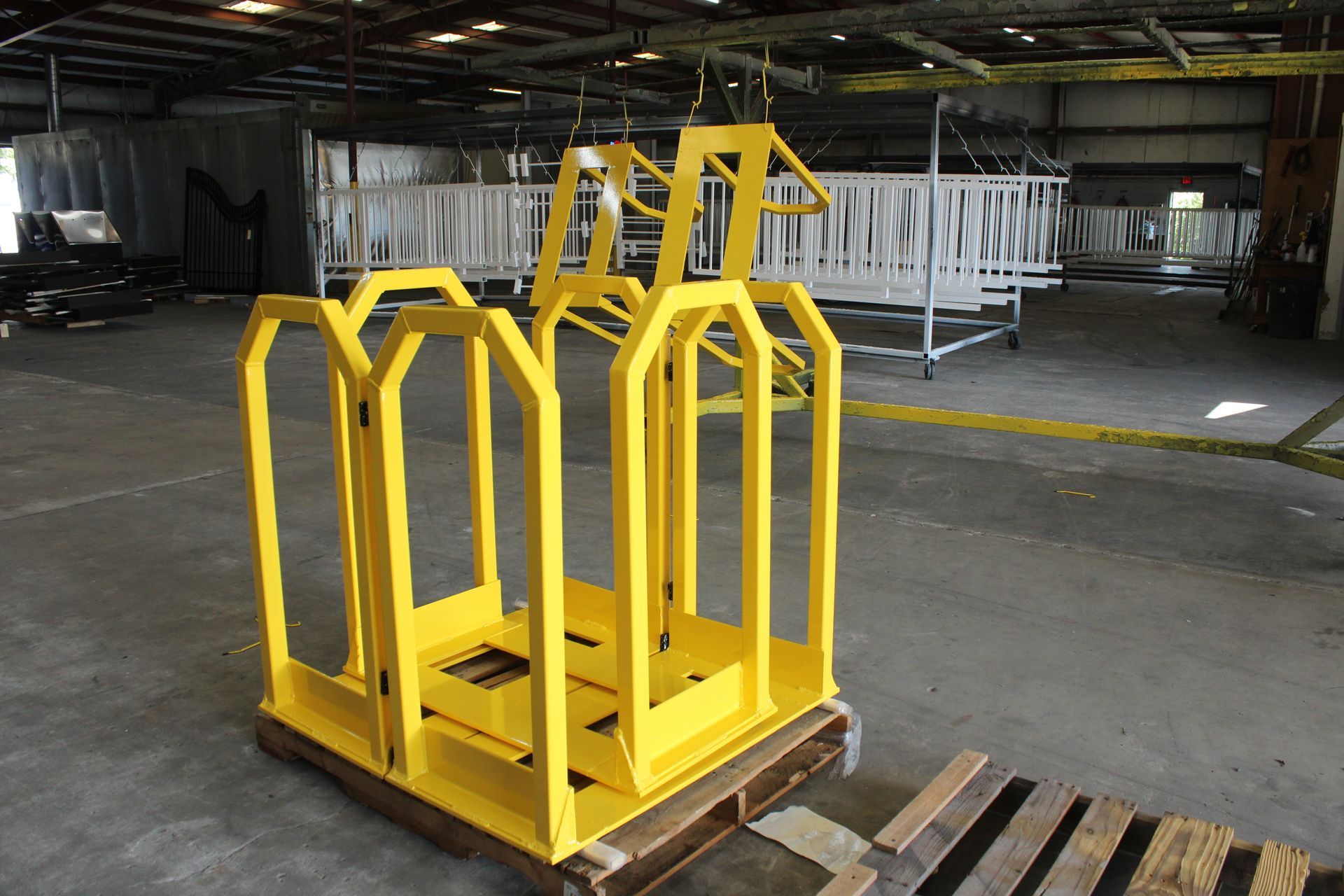 Yellow metal cages on a pallet in a warehouse, with other white painted metal structures in the background.