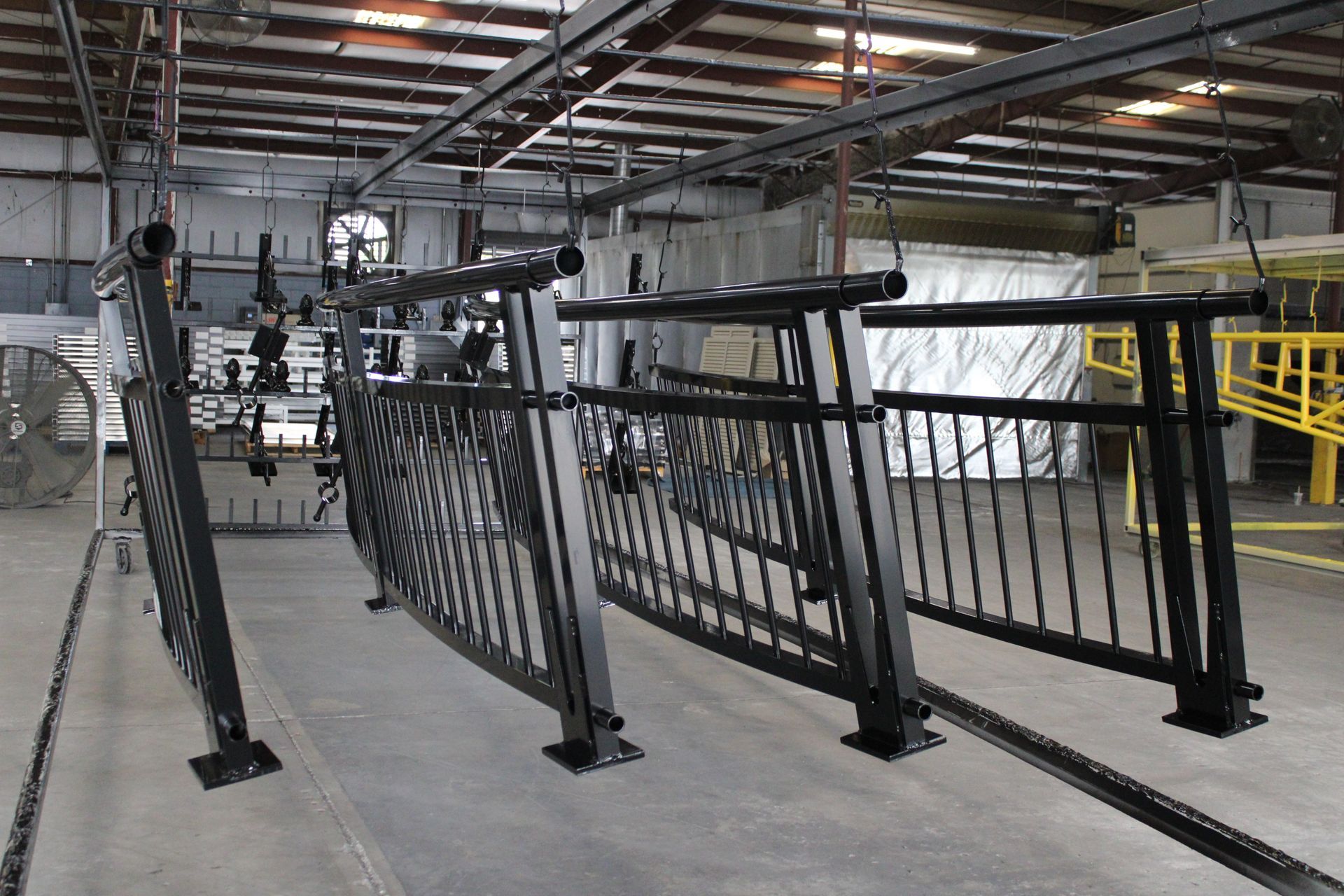 Black metal railings hanging in a factory, suspended from an overhead track.