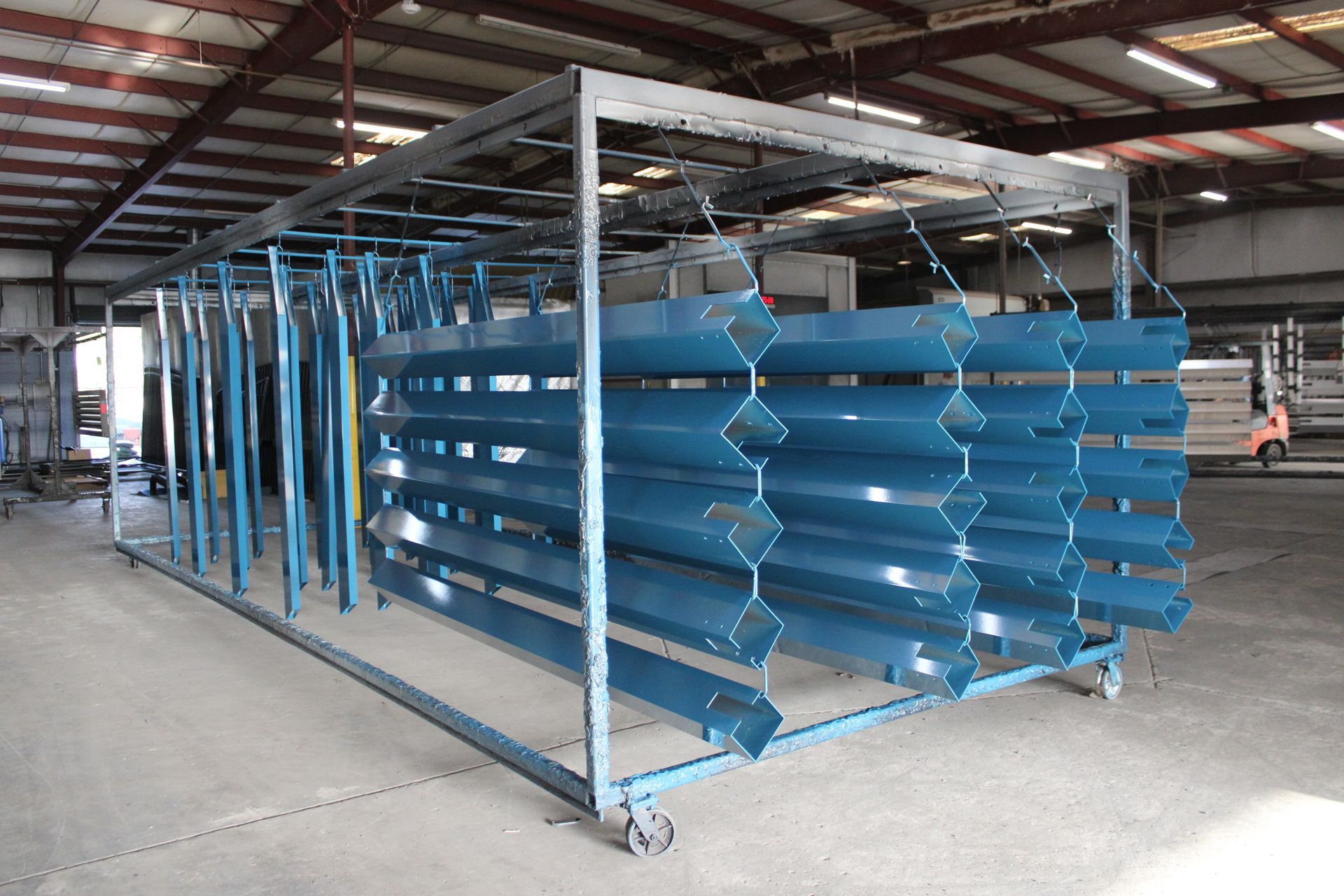 Blue painted metal parts hanging on a rolling rack inside a warehouse.