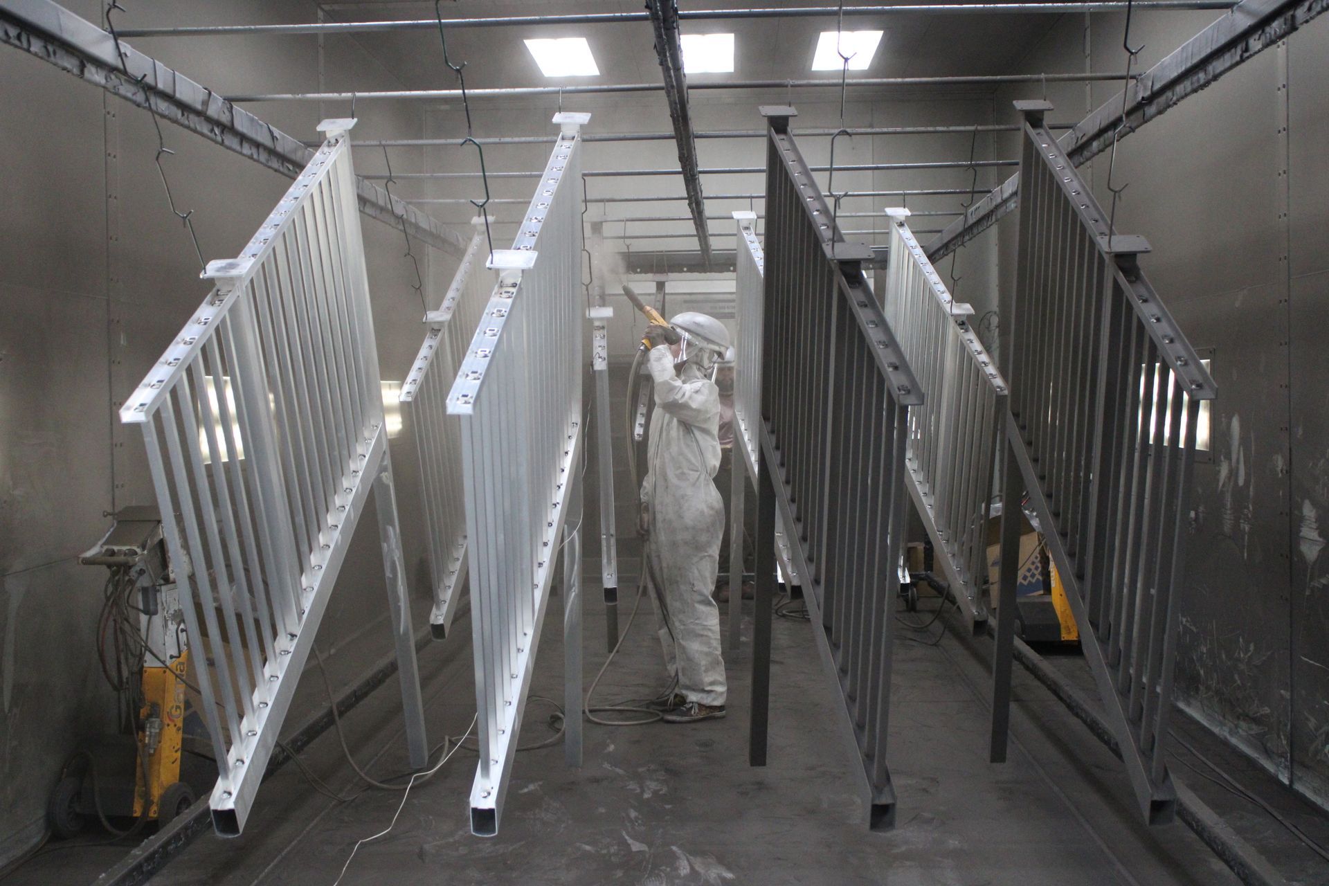 Person in protective suit spraying paint on metal railings in a spray booth.