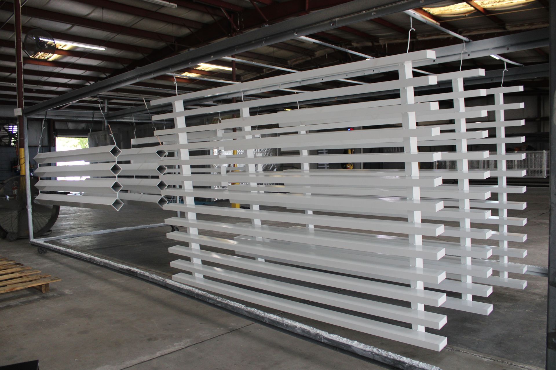 White painted metal pieces hanging on a rack in a factory setting.