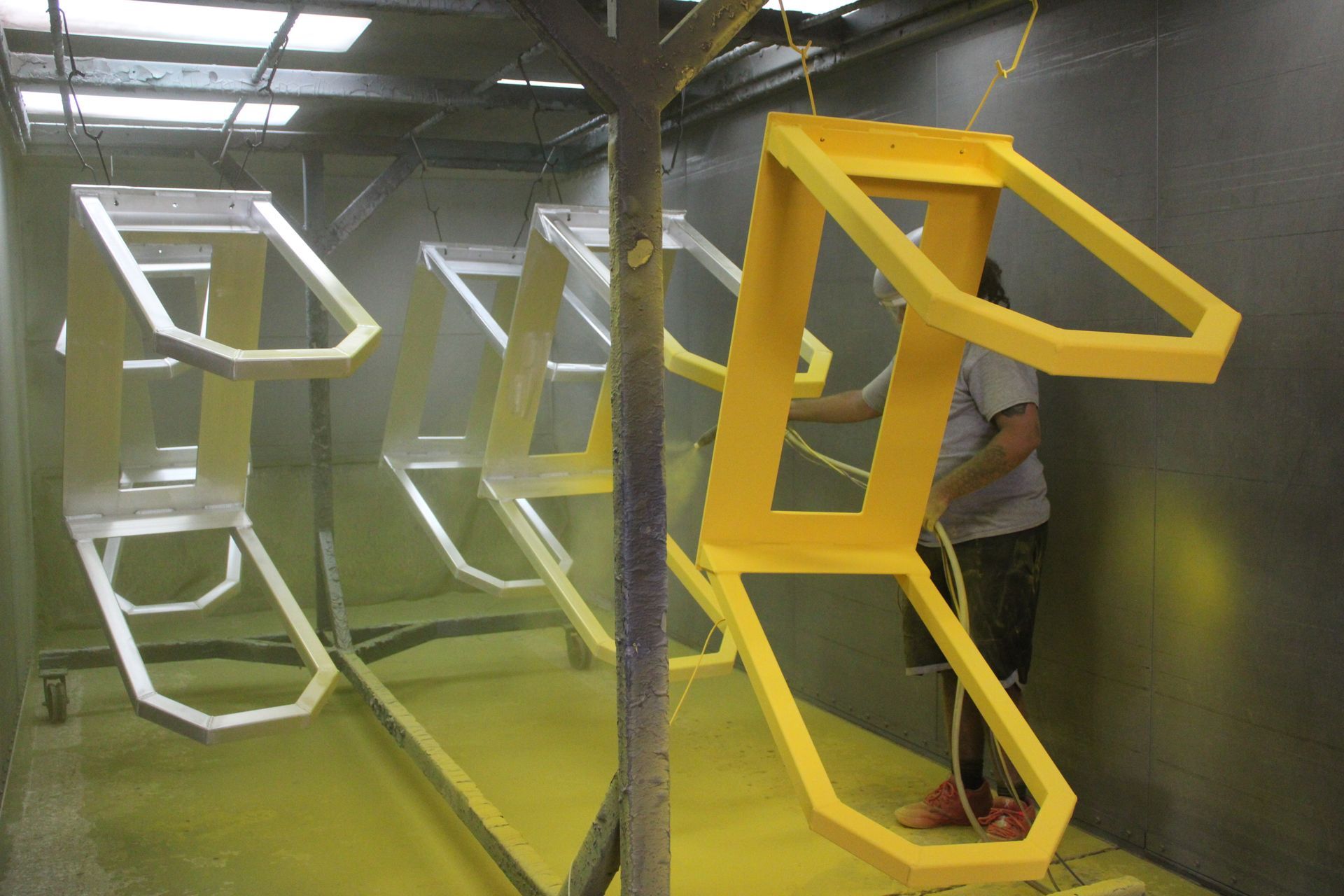 Person spray painting yellow frames in an industrial setting. Some frames are white.