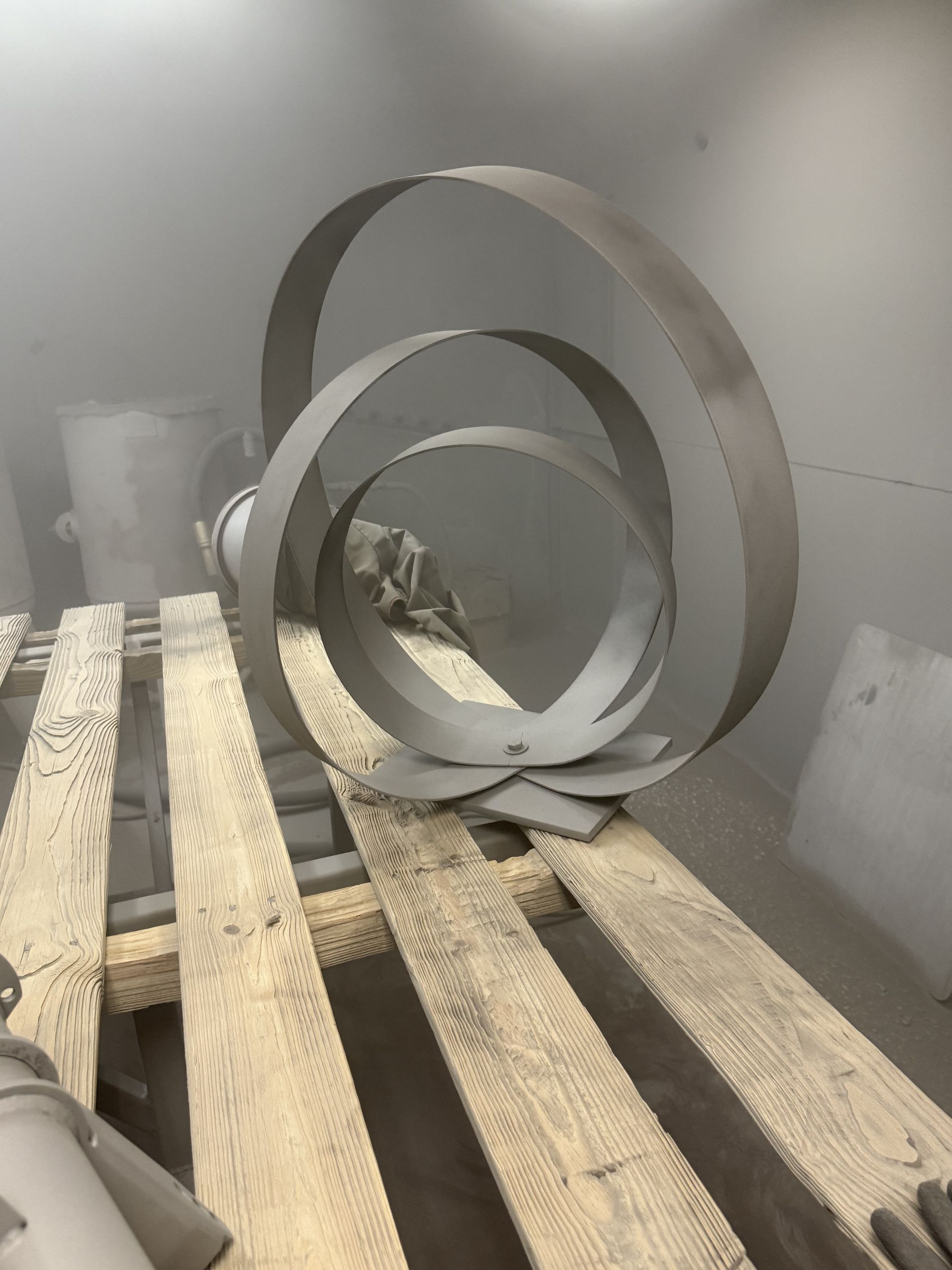 Dusty workshop with two large metal rings leaning against a wall on a wooden pallet