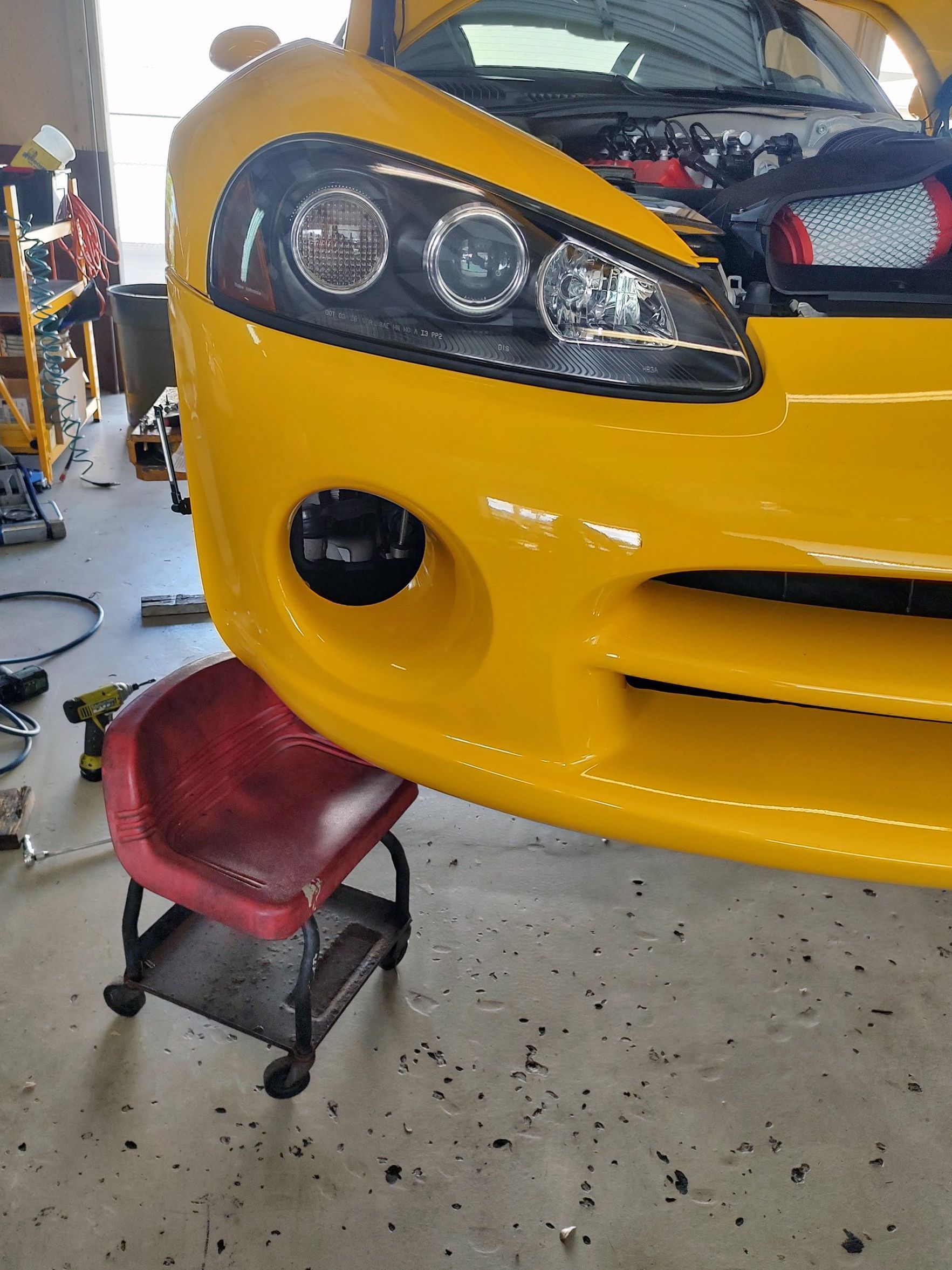 Yellow Dodge Viper car front bumper, headlights, and fog light, raised on a red shop stool.