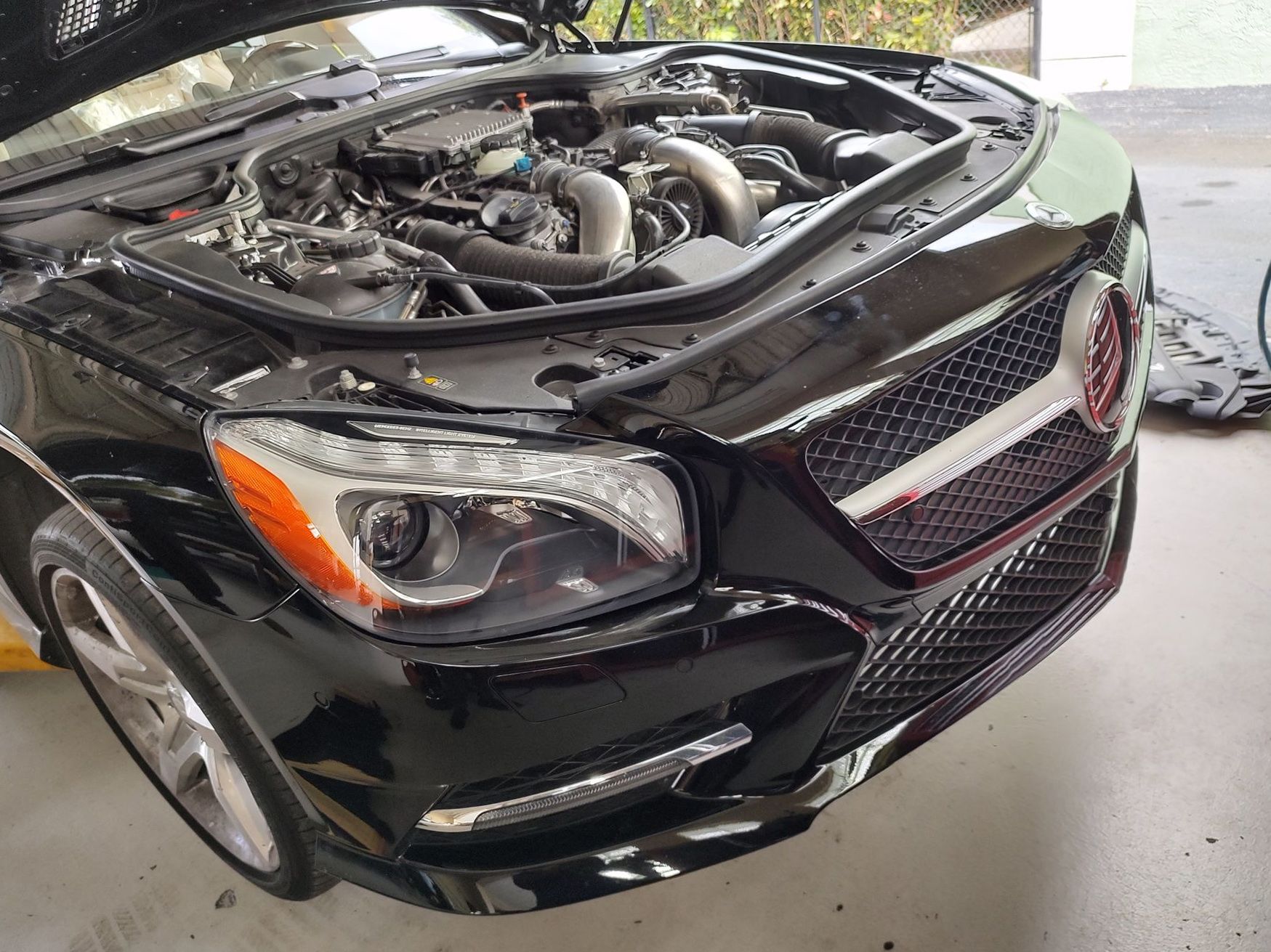 Black Mercedes-Benz car with open hood in a garage. Shiny exterior, visible engine components.