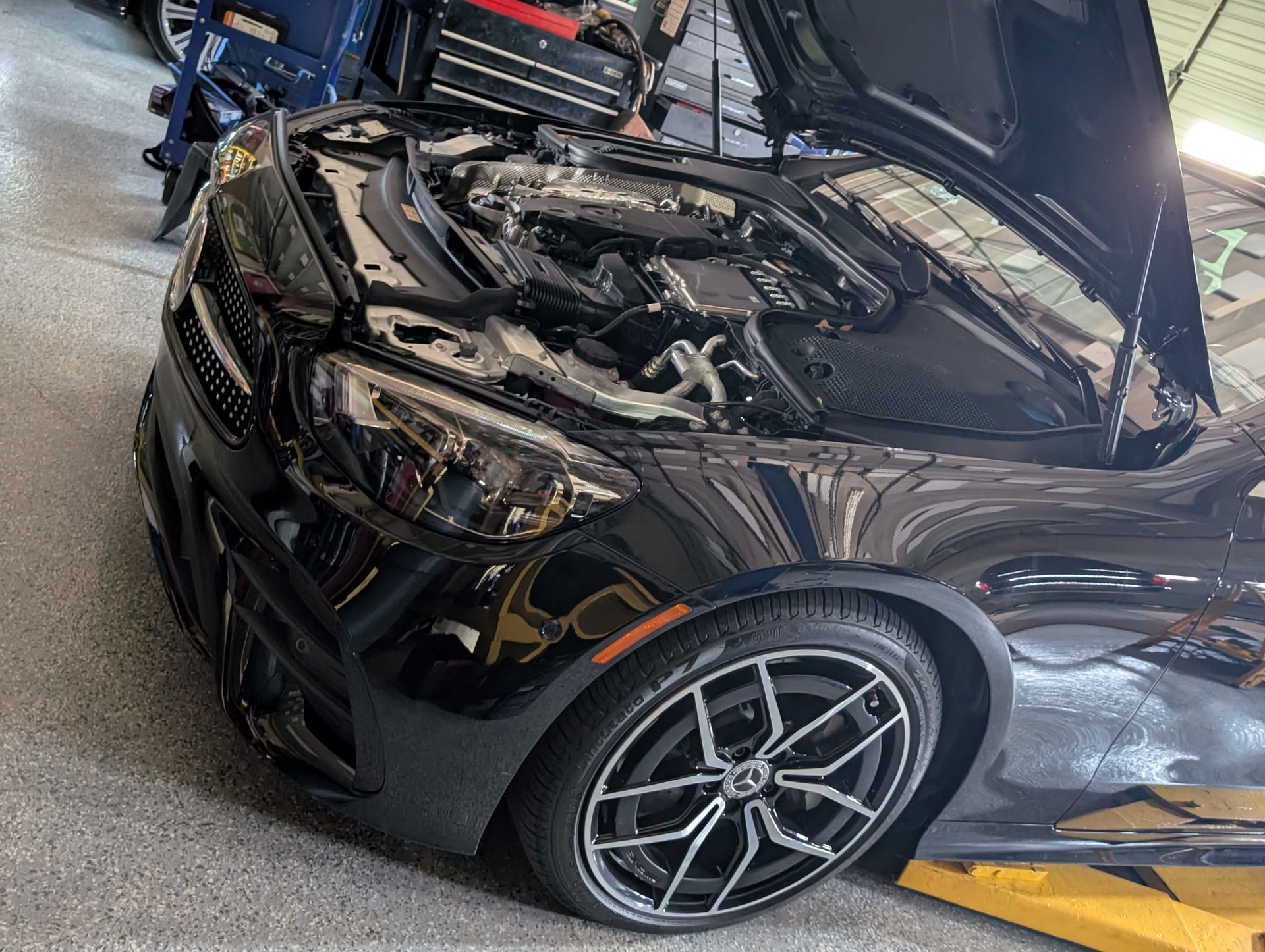 Black car with hood open in a garage; shows engine and front tires.