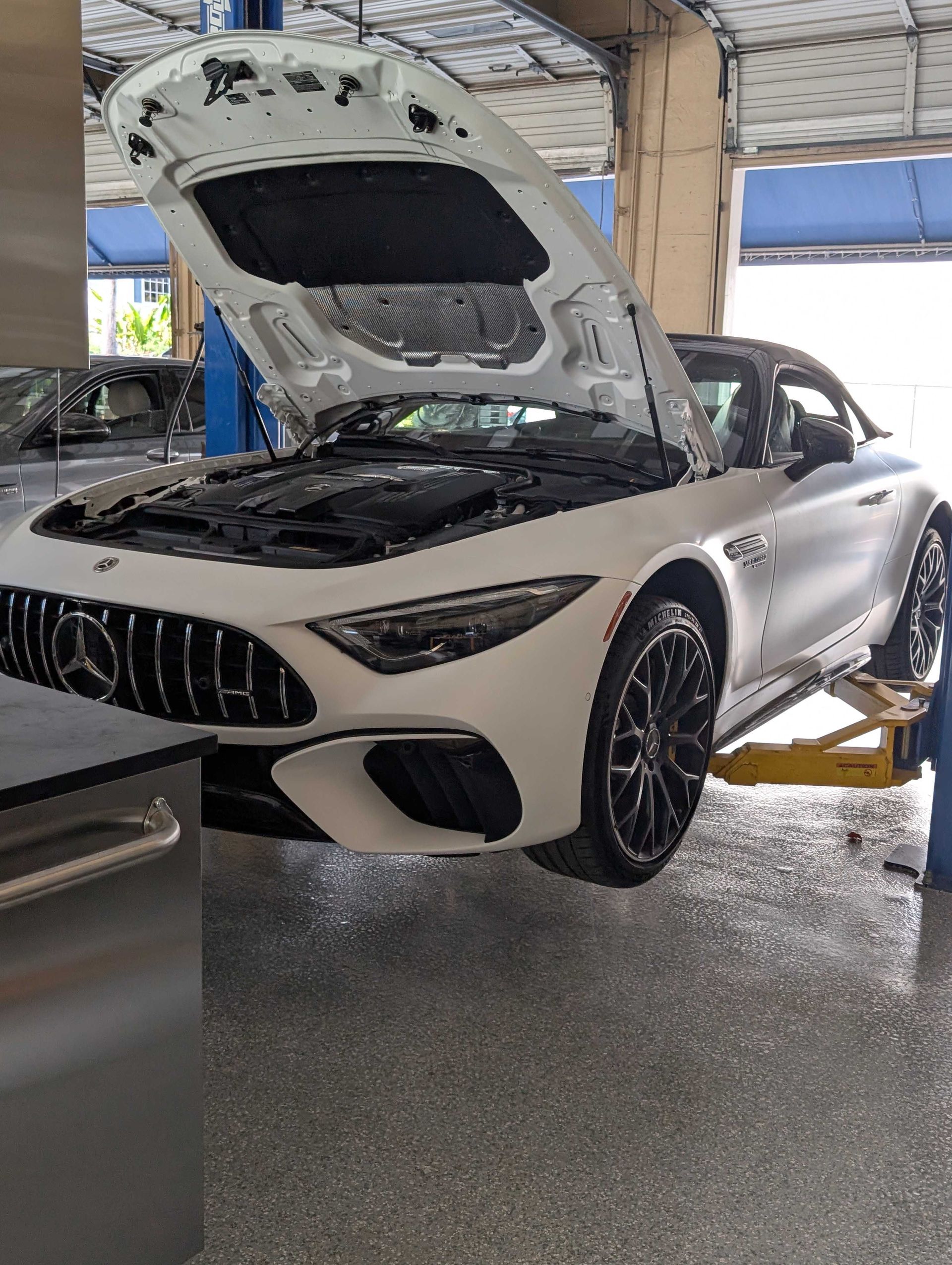 White Mercedes SL AMG on a lift with hood open in a garage.