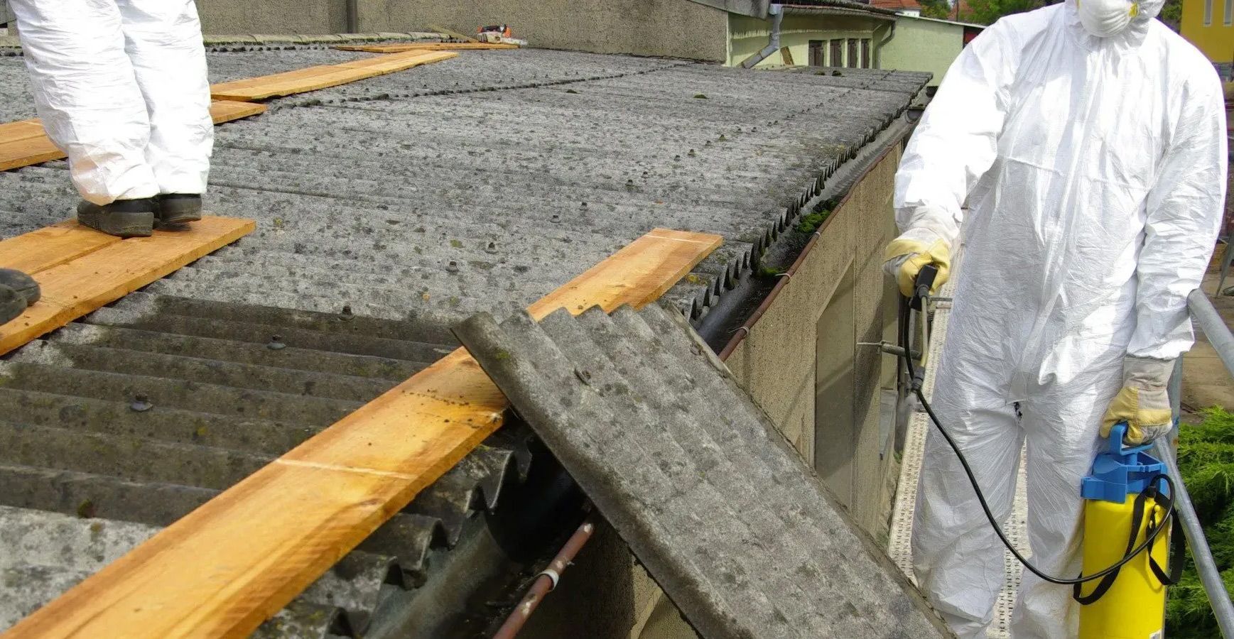 A man in a white suit is spraying a roof with a vacuum cleaner.