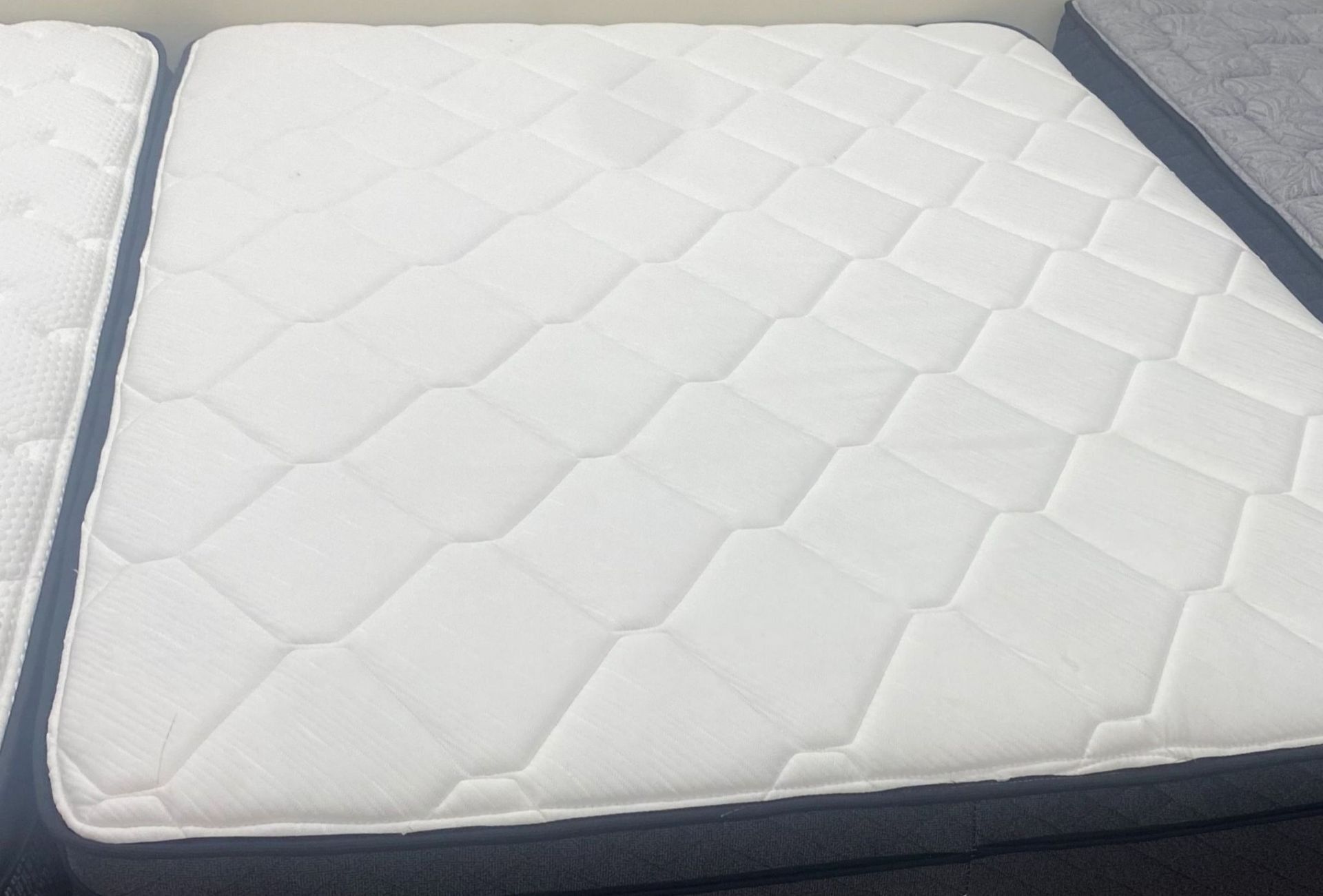 White quilted mattress with dark gray border, displayed on a bed frame.
