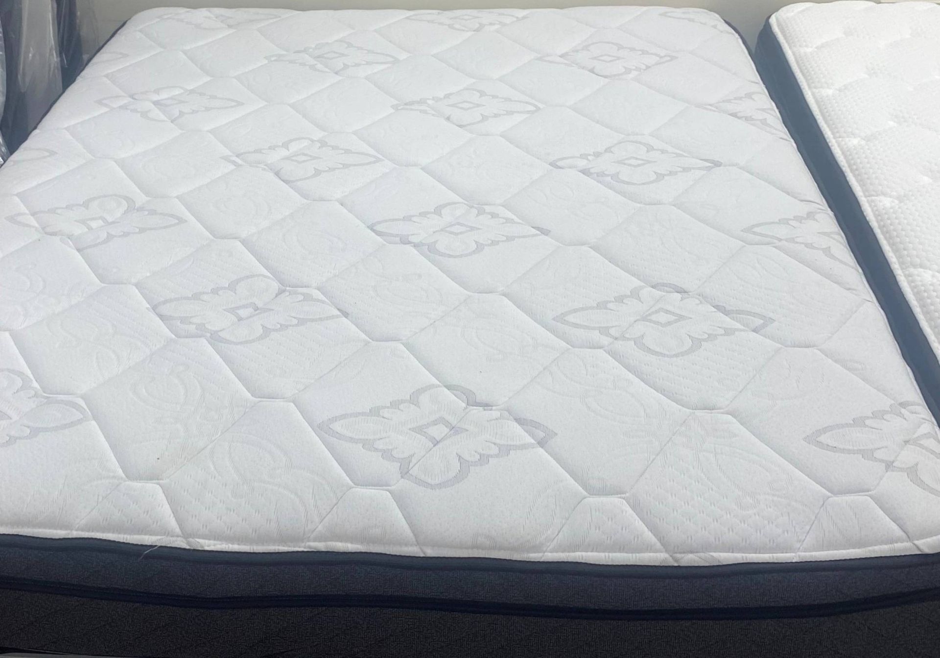 White quilted mattress with dark gray border, sitting on a bed frame.