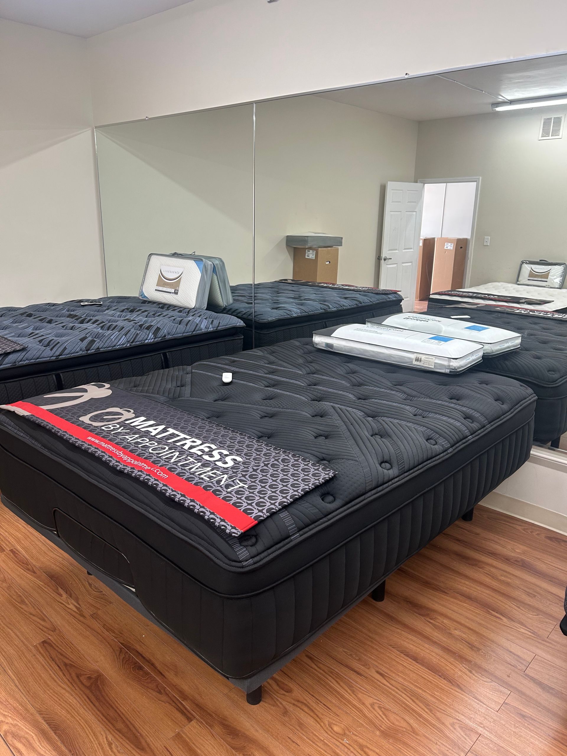 Mattresses of various colors displayed in a room with a mirror and wooden flooring